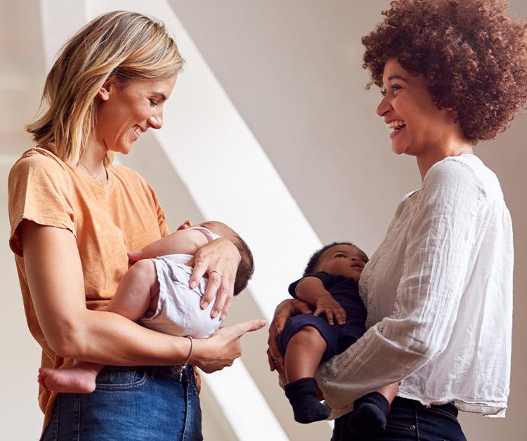 Two moms holding their sleepy babies and talking