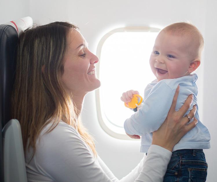 A mother holding her smiling baby on an airplane near the window.