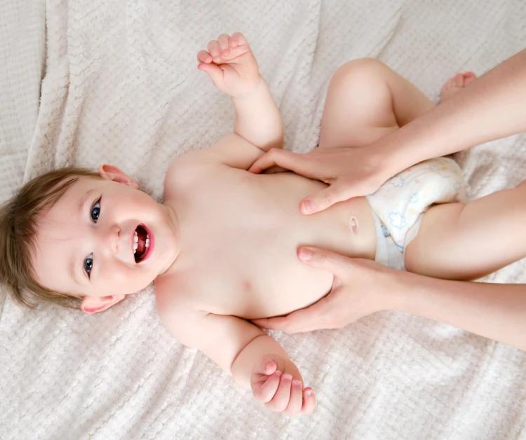 Baby laying on their back with a big smile as mom holds his tummy