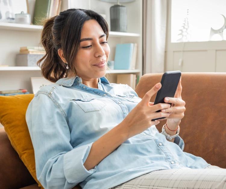Madre embarazada tumbada en el sofá mirando el teléfono