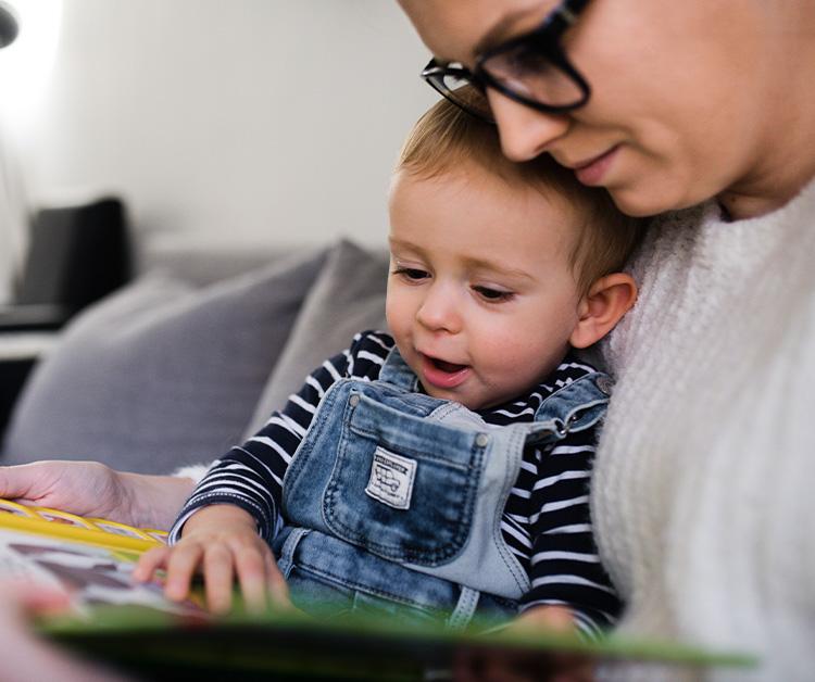 Niño sentado en el regazo de su madre y leyendo un libro