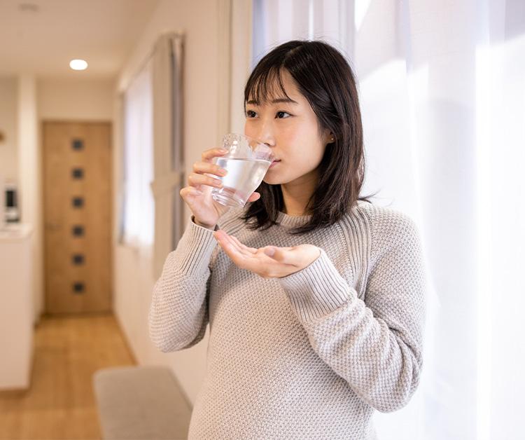 Pregnant woman drinking a glass of water and holding a vitamin