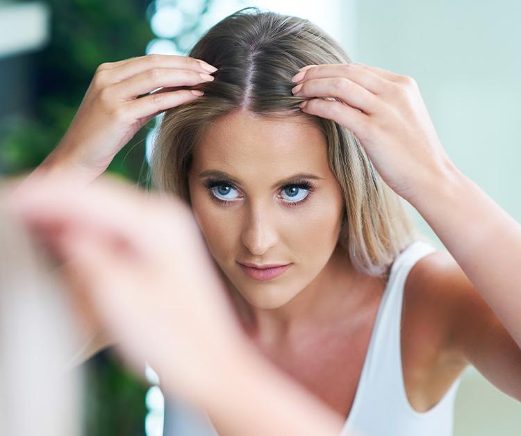 Woman looking closely at her hair in the mirror
