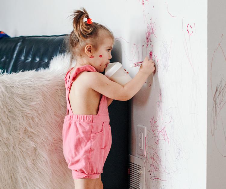 Toddler with sippy cup coloring on wall