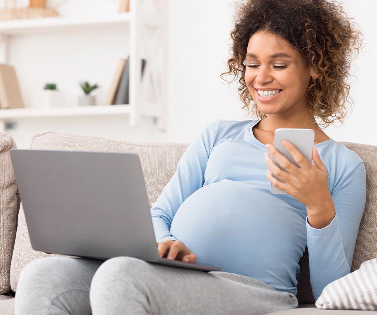 Pregnant woman sitting on the couch using her laptop and phone