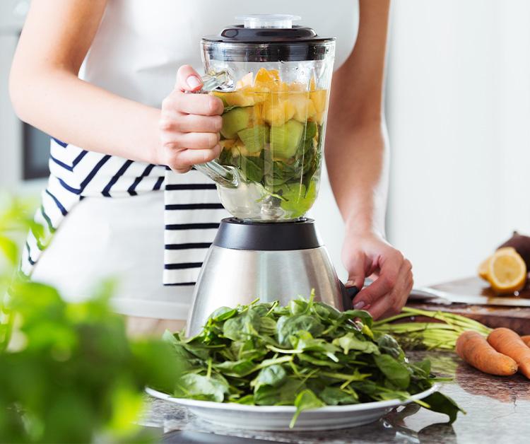 Mujer poniendo verduras en una licuadora