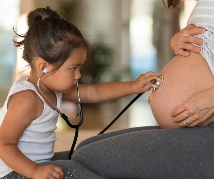 Pregnant mother with toddler using a stethoscope on her belly