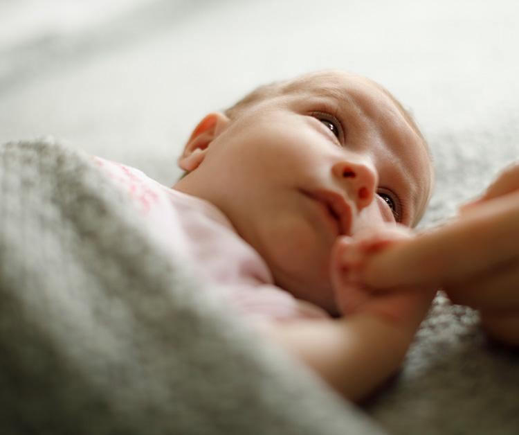 Newborn holding mom's finger while looking at her