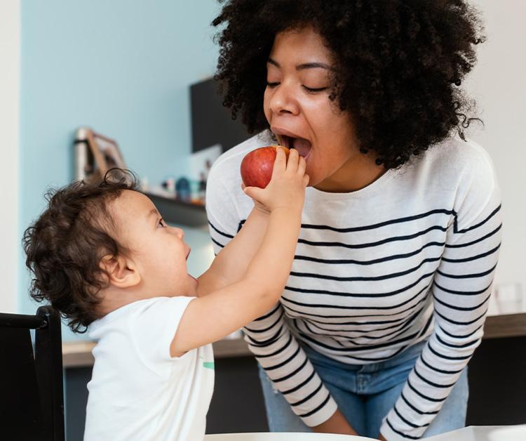 Baby trying to feed his mom an apple