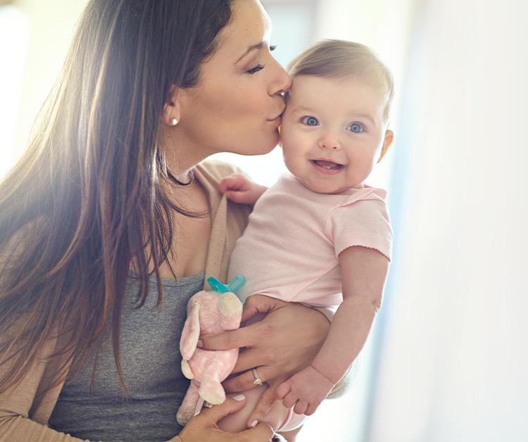 Mom holding her smiling daughter and kissing her on the cheek