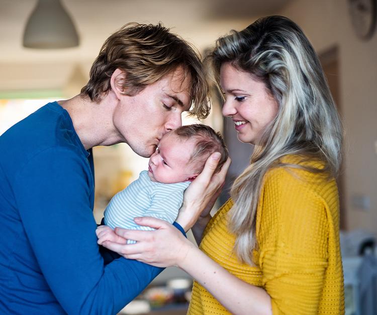 Dad kissing newborn's forehead while mom watches