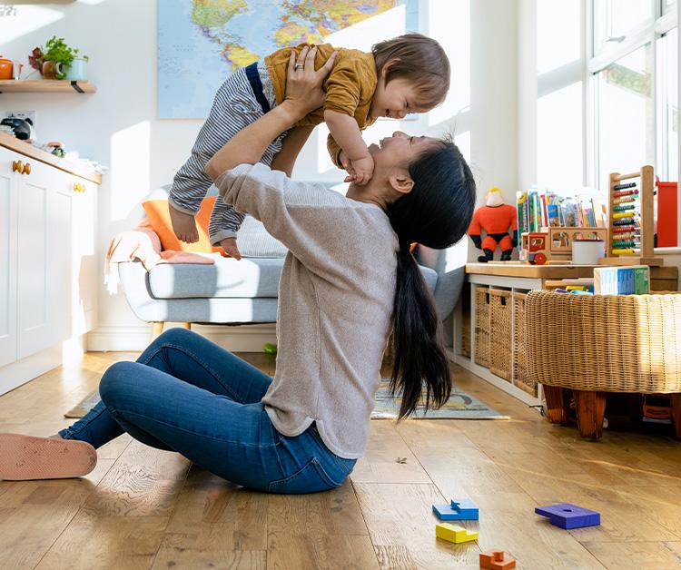 Mom smiling and holding toddler up in the air while they play