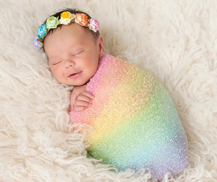 Smiling sleeping baby swaddled in a rainbow blanket and wearing a rainbow headband