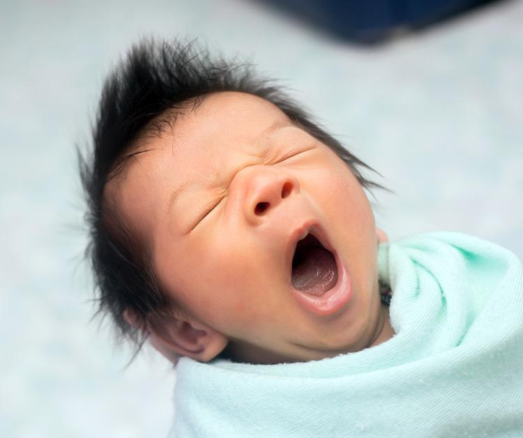 Mom holding yawning baby in her lap