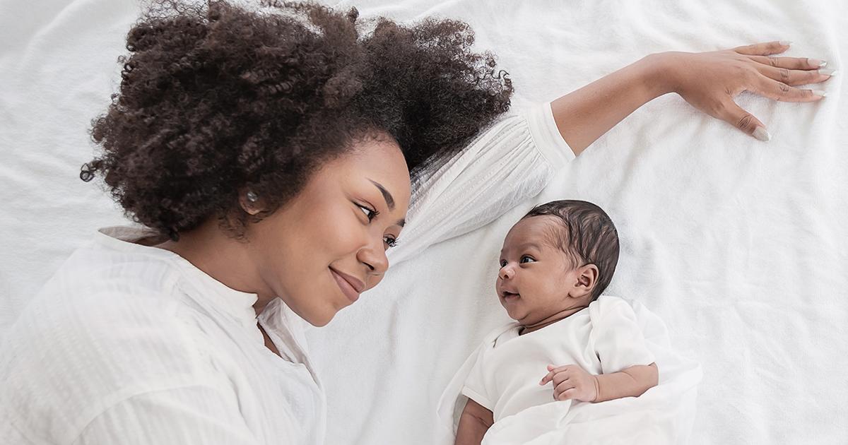 Mom laying on a bed looking lovingly at newborn infant