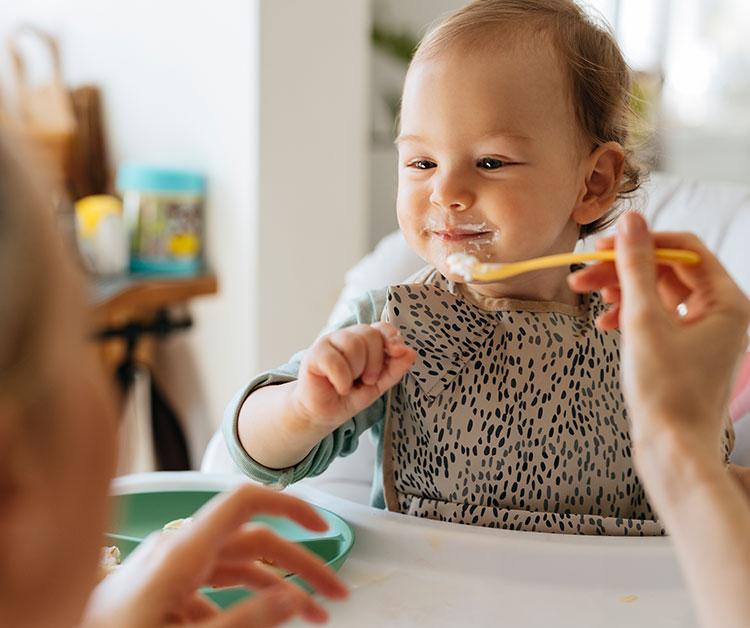 Mom feeding a baby in a highchair with a spooon