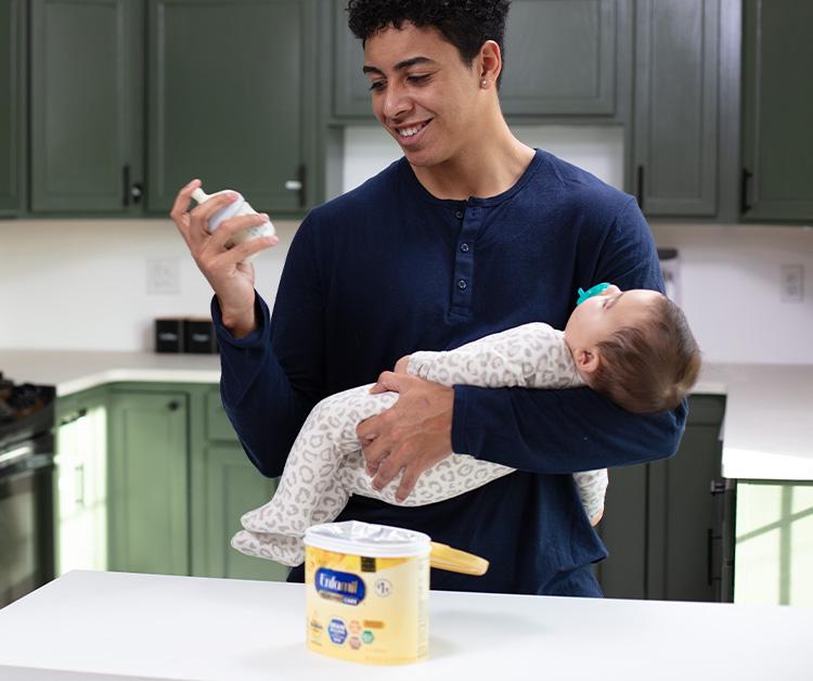 Dad checking bottle while cradling baby