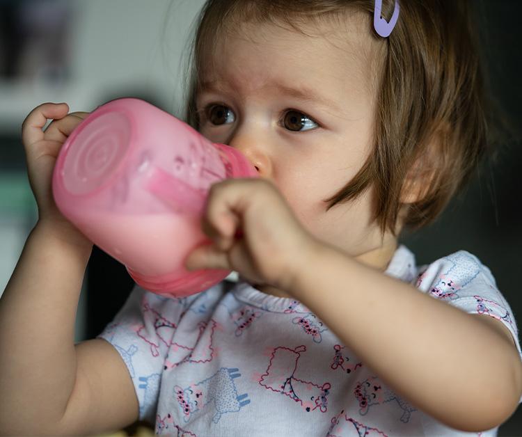 Smiling toddler girl sitting at a table with a plate and sippy cup